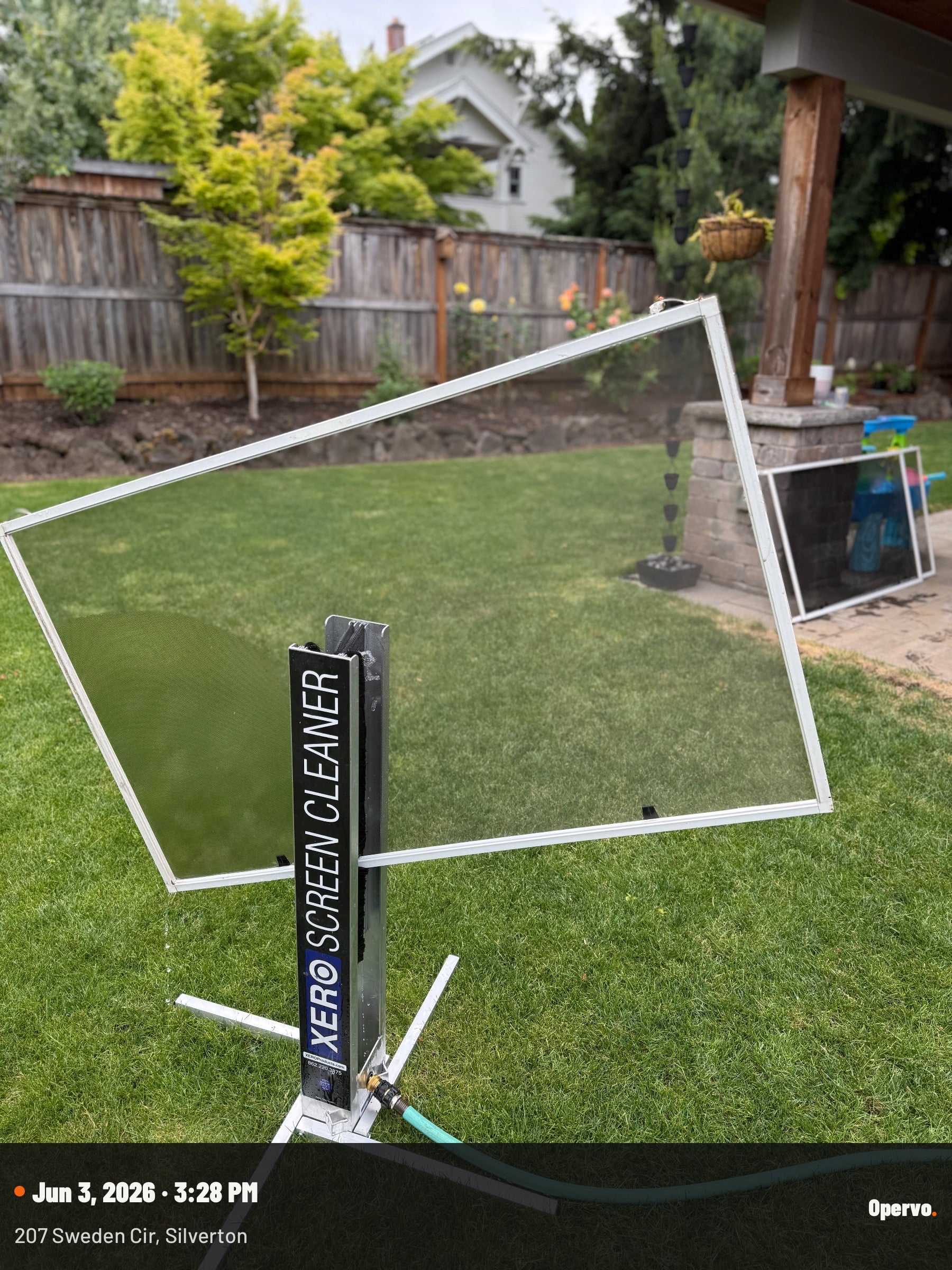 XERO screen cleaning machine set up in a backyard with a window screen mounted on it.